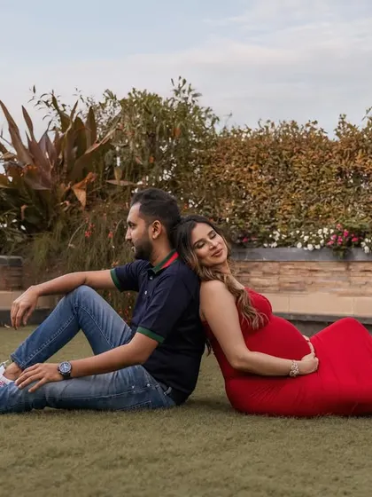 A relaxed outdoor portrait. The couple sits back to back on a lush green lawn, creating a symmetrical and peaceful image that captures a quiet moment of togetherness.