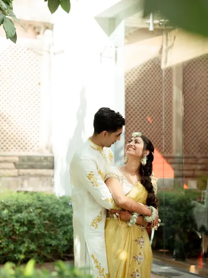 A tender moment between the couple during their Haldi ceremony photoshoot in Udaipur. The lush green background complements their traditional yellow outfits perfectly.