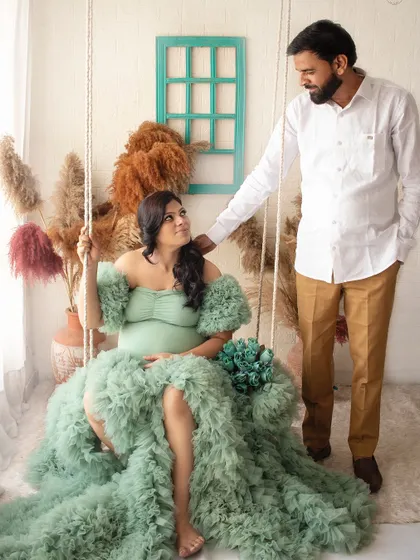 A dreamy maternity portrait on a studio swing. The flowing green dress and boho setup create a whimsical and romantic scene.