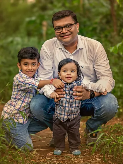 A father crouches down with his two young sons for a family portrait in the woods. The image showcases a proud father with his boys, surrounded by the calm of nature.