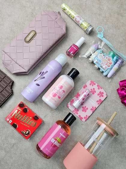 A flat lay of the items included in our sister's Rakhi hamper. It features a mix of skincare, cosmetics, a glass tumbler, and sweet treats for a complete pampering experience.