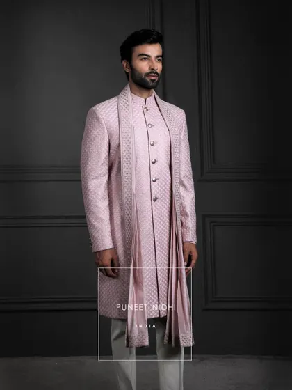 Soft as dawn, regal as legacy. This pink silk sherwani blooms with jacquard finesse, layered with a fish-scale achkan and stole, carrying tradition with graceful majesty.