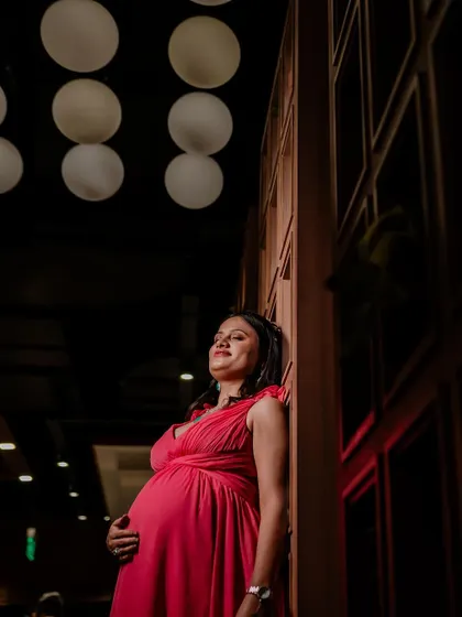 This is a beautiful solo maternity portrait focusing on the mother-to-be. The dramatic lighting from the side and above creates an artistic feel, highlighting her silhouette and joyful, serene expression.