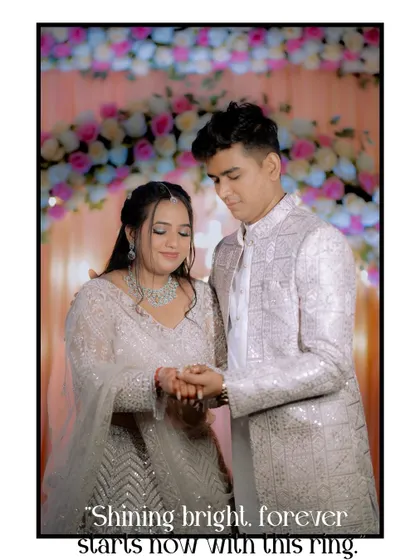 The couple looks down at their hands right after the ring exchange, with a floral backdrop. The text overlay adds a touch of modern romance to this classic engagement photo.