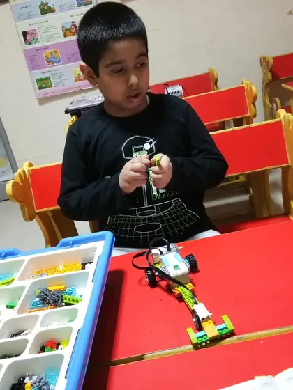 A student focuses on assembling a LEGO WeDo robot, connecting the motor and sensors. He is learning the basics of robotic construction and programming.