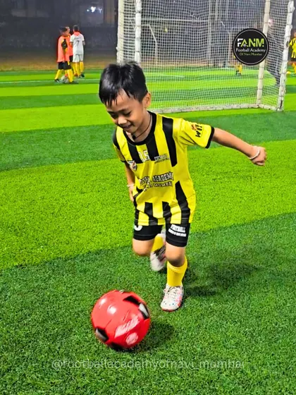 The joy of the game starts here. A young player runs with a smile on his face, chasing a bright red ball during a fun drill.