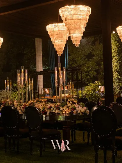 An elegant dining table with a mirrored top, reflecting the floral runner and the unique, modern chandeliers above. The black chairs add a touch of formal sophistication.