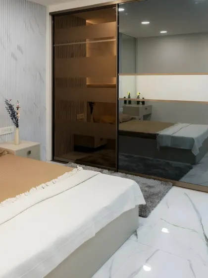 This tinted glass sliding wardrobe offers a sophisticated way to store your belongings. The semi-transparent doors, paired with fluted wall panels and soft lighting, create a luxurious and serene bedroom retreat.