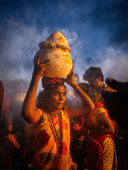 A woman carries a decorated pot on her head through a cloud of smoke during Kulasai Dasara, her face a picture of determination and faith.