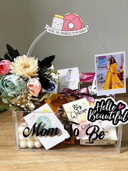 Celebrating a new chapter with a 'Mom to Be' hamper! This acrylic basket is filled with goodies like chocolates, skincare, and a bubble candle, all topped with a custom polaroid and cute decorations to pamper the new mommy.