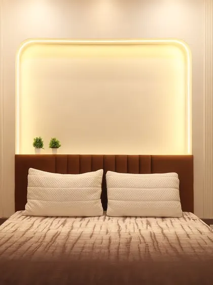 This bedroom features a backlit wall niche with rounded corners, creating a soft and modern focal point above the bed. The design is complemented by a simple upholstered headboard and minimalist bedside tables.