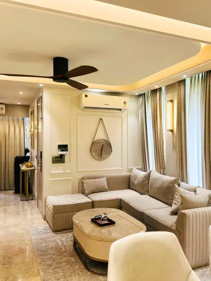 A full view of a living room designed with a neutral color palette, featuring a comfortable sectional sofa, classic wall molding, and soft, layered lighting.