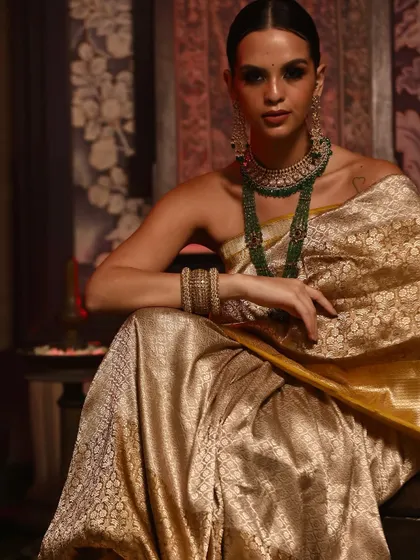A close-up portrait of a model in a golden Banarasi saree, highlighting the intricate weaving and stunning emerald jewellery.