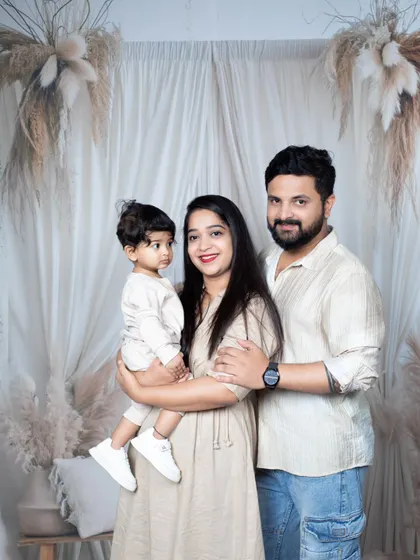 A classic family portrait of a mother, father, and their baby boy, all dressed in coordinated beige outfits.
