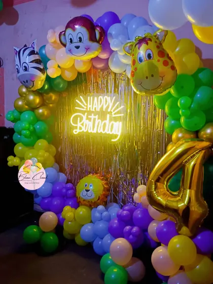 A colorful jungle-themed balloon ring with animal foils and a neon 'Happy Birthday' sign, perfect for a 4th birthday.