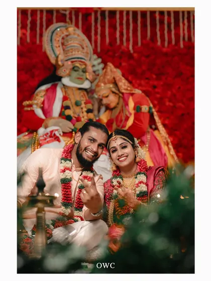 A fun shot of the couple making heart gestures with their hands, posing with Kathakali dancers.