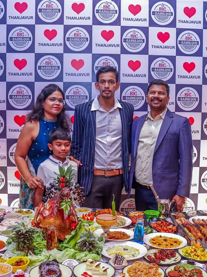 A family poses in front of our grand feast, highlighting how our catering turns any event into a memorable celebration. The table is packed with everything from biryani and curries to kebabs and desserts.