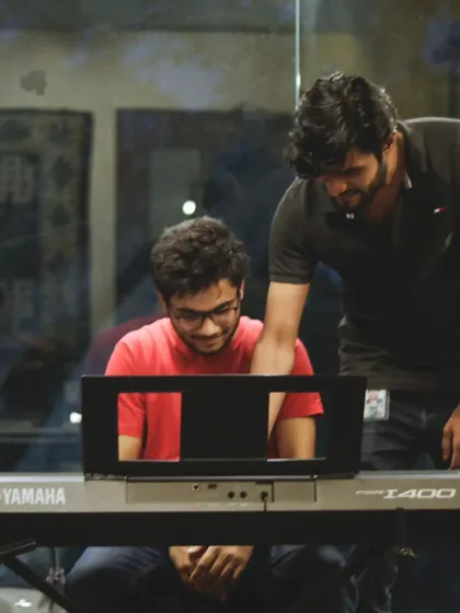 A teacher providing one-on-one guidance at the keyboard during a group workshop. We make sure every student gets the attention they need to succeed.