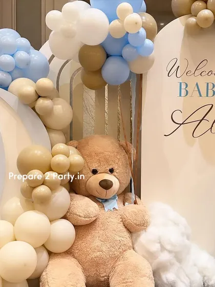A detailed view of the large teddy bear nestled among cream and blue balloons, with fluffy white cloud props adding a dreamy touch to the welcome baby decor.