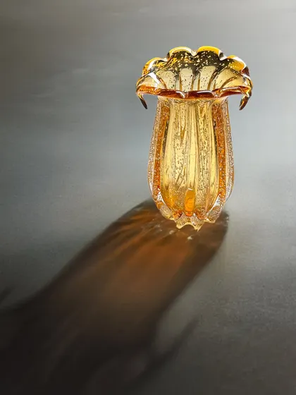 Where light dances on glass. This amber-toned, fluted glass vase casts a beautiful, dramatic shadow, showcasing its intricate texture and form. It is the art piece your home has been waiting for.