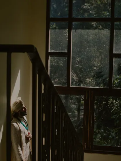 A pensive groom's portrait at Oleander Farms, using natural light from a window to create a moody and artistic shot.