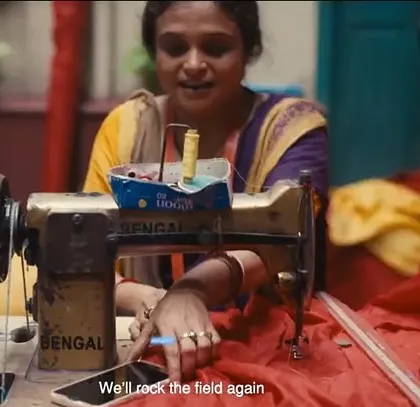 A touching scene from the East Bengal FC film, where a woman is sewing a team flag. Her simple saree and the vibrant colors of the fabric tell a story of community and support.