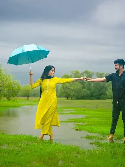 A romantic pre-wedding photograph of a couple in a beautiful green meadow. The use of a simple prop like an umbrella adds a touch of charm and storytelling to the image.