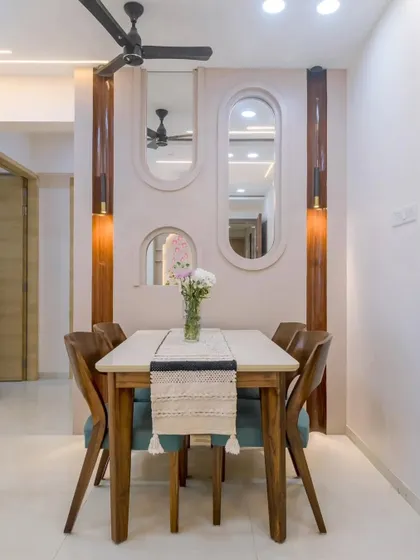 A cozy dining nook featuring a wooden table and chairs with teal upholstery. The wall is adorned with multiple arched mirrors of varying sizes, creating an interesting visual element and making the space feel larger.