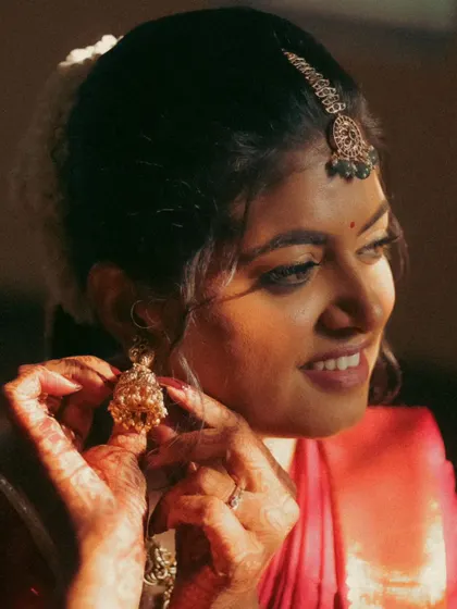 A close-up shot of a bride adjusting her earring. The warm, directional light highlights the details of her henna and jewelry, capturing a quiet, intimate getting-ready moment.
