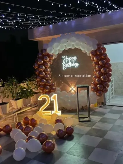 A chic terrace party for a 21st birthday. The decor includes a fairy light canopy, a rose gold and white balloon arch, and a '21' marquee number.
