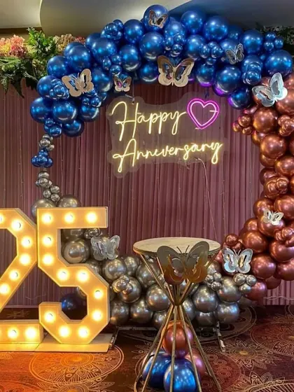 A grand 25th-anniversary celebration with a balloon ring in blue, silver, and copper, butterfly accents, and large marquee numbers.