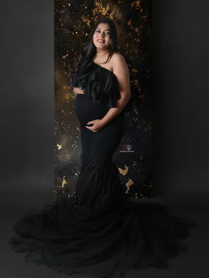 Embodying strength and elegance in a striking black one-shoulder gown. The textured gold and black backdrop adds a layer of drama and sophistication to this studio maternity portrait.