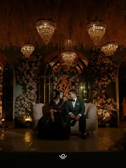 A wide shot of a couple on their reception stage, surrounded by opulent floral decor and chandeliers, showcasing the grandeur of the event.
