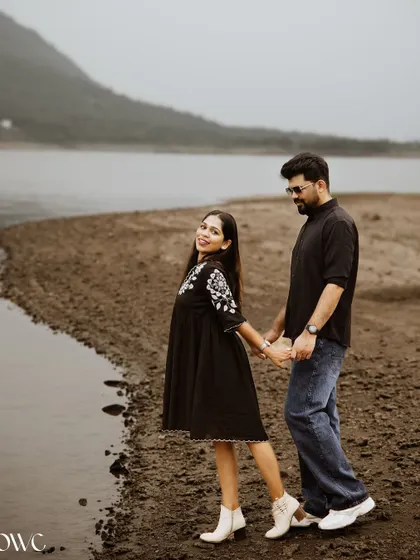 A classic "follow me" shot along a lakeshore, with the couple looking back at the camera with smiles.