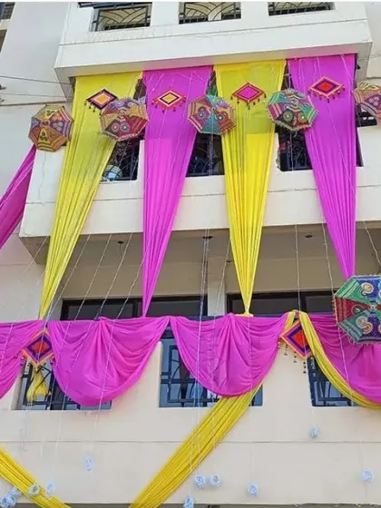 The balcony of a building decorated with pink and yellow drapes and colorful Rajasthani umbrellas for a Mehendi function.