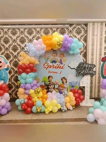 A colorful Cocomelon first birthday party. This setup features a backdrop with all the Cocomelon characters and a multi-colored balloon arrangement.