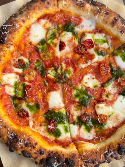 A vibrant Sundried Tomato & Basil pizza, sliced into perfect portions. The colors of the Italian flag, red, white, and green, are all here.