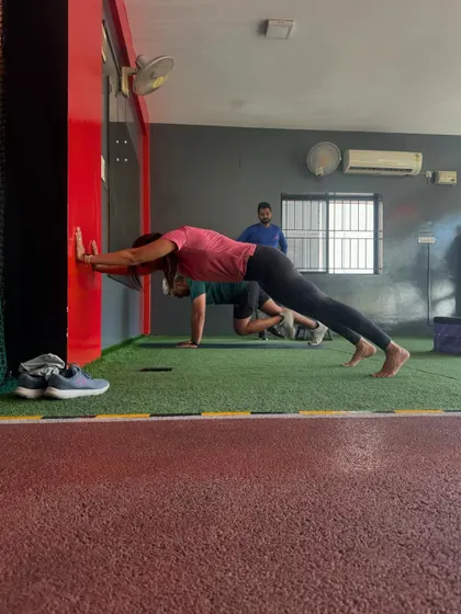 A client holds a plank against a wall, an isometric exercise that builds core endurance and shoulder stability.