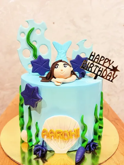 A simple and sweet mermaid-themed cake with a fondant mermaid peeking out of the water.