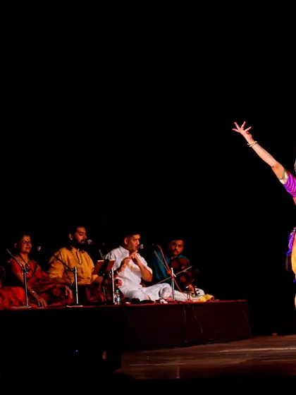 A wider view of the orchestra and dancer on stage. The visual of the artists together shows the collaborative nature of a Bharatanatyam recital.