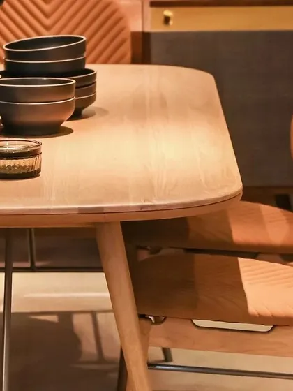 A detail shot of the Volta Oak Dining Table's surface and the accompanying chairs. The natural grain of the solid oak and the precise stitching on the upholstery are testaments to our commitment to quality craftsmanship.