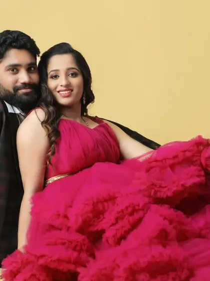 A cozy and romantic studio portrait of an expecting couple. The rich color of the magenta gown contrasts beautifully with the simple yellow background.
