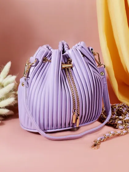 This image showcases a trendy purple bucket bag against a soft, two tone background. The styling with flowing fabric and delicate pampas grass adds a touch of elegance and softness.