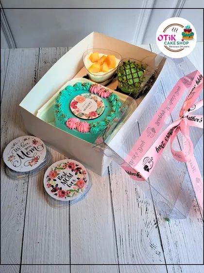A Mother's Day hamper box including a floral-themed bento cake, a mango mousse cup, and a pistachio treat, complete with "Best Mom Ever" coasters.