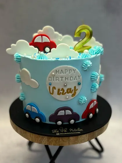 A cute car-themed cake for a second birthday. Fondant cars drive around the light blue buttercream, with fluffy clouds adding to the sky-high fun.