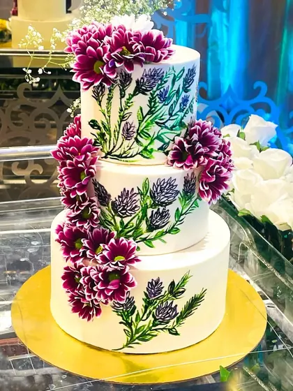 A beautiful example of a hand-painted floral wedding cake. This three-tier design features delicate painted greenery and is accented with vibrant fresh flowers for a whimsical, romantic look.