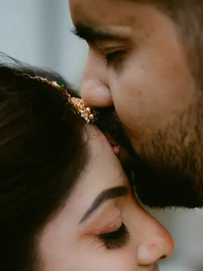 A close-up shot capturing the intimacy of a forehead kiss. The focus on the bride's maang tikka and the groom's touch is incredibly romantic.