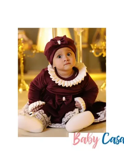 This little girl looks like a vintage doll in her deep maroon velvet dress with a ruffled white collar. It's a perfect, elegant outfit for a winter celebration or photoshoot.