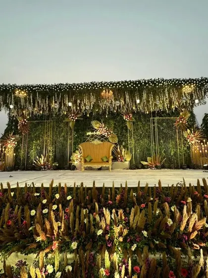 This wide shot captures the full splendor of the reception stage. The combination of a green wall, hanging florals, and a foreground of pampas grass creates a rich, layered, and utterly luxurious visual.