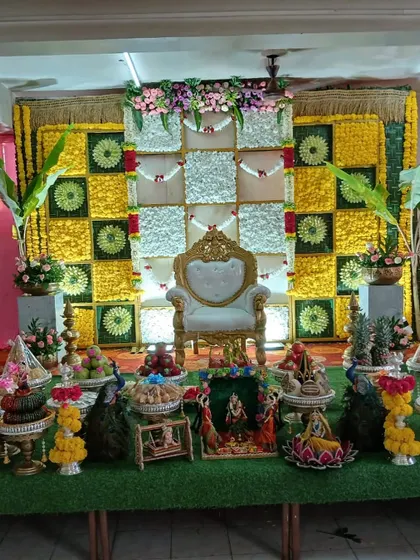 An elegant offering display featuring decorative peacocks and traditional dolls. This setup is placed in front of a classic checkerboard floral backdrop, creating a complete and picturesque scene.